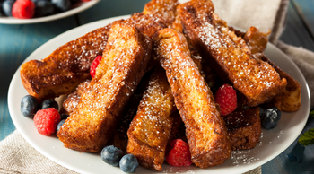 French toast sticks with berries and powdered sugar on a white plate.