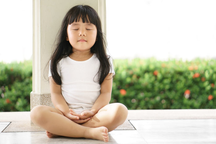 young girl sitting calm cross legged with eyes closed 